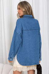 A woman wearing an oversized blue denim shirt jacket, shown from the back, paired with a cream lace-trimmed skirt, standing in front of white curtains.