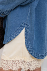 Close-up of a person wearing a blue denim shirt layered over cream-colored shorts with a lace hem.