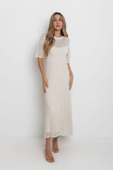 Woman wearing a long, light-colored dress with a white background