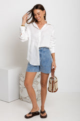 Woman wearing a white shirt and denim shorts holding a beige handbag on a white background