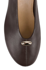 A close-up top-down view of a dark brown leather flat shoe with a small metallic gold accent on the toe, set against a plain white background.