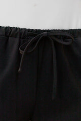 Close-up of black drawstring pants showing the elastic waistband and black drawstring tie.