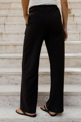 A person wearing black wide-leg drawstring pants and black sandals, standing on light stone steps.