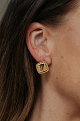 Gold earring worn by a person with brown hair.
