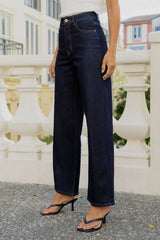 A person wearing dark blue wide-leg jeans with a white top and black heeled sandals, standing outdoors in front of a white balustrade railing.