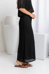 A model wearing a midi length black crochet knit skirt with a ribbed elastic waistband and fitted silhouette.