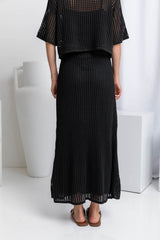 A model wearing a midi length black crochet knit skirt with a ribbed elastic waistband and fitted silhouette.