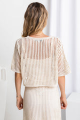 A female model wearing a beige crochet crop top with a scoop neckline and 1/4 sleeves.