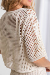 A female model wearing a beige crochet crop top with a scoop neckline and 1/4 sleeves.