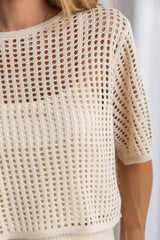 A female model wearing a beige crochet crop top with a scoop neckline and 1/4 sleeves.