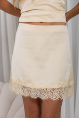A close-up of a model wearing a cream satin mini skirt with a lace hem, paired with a matching satin crop top.