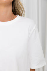 Close-up of a person wearing a plain white short-sleeve crew-neck T-shirt against a light neutral background.