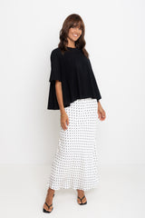 Woman wearing a black top and white patterned skirt on a white background