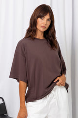 Woman wearing an oversized brown t-shirt with white pants, on a white background.