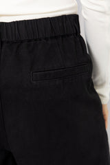 Woman wearing a white long-sleeve top with black tailored trousers, carrying a brown suede bag, on a white background.