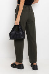 Person wearing olive green pants holding a black bag against a white background