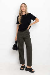 Woman wearing a black t-shirt and green pants holding a black handbag on a white background