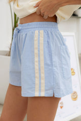 A person wearing light blue drawstring shorts with two vertical cream stripes and a side pocket, cropped from the waist down in a bright indoor setting.