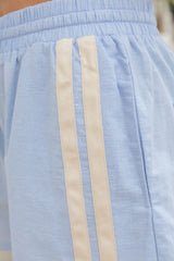 Close-up of light blue athletic shorts with two vertical cream stripes down the side and an elastic waistband.