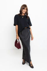Woman wearing a black top and patterned skirt with a maroon handbag on a white background