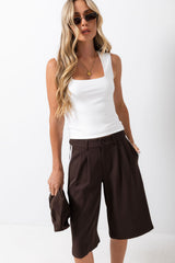 A woman modeling a white sleeveless tank top and dark brown wide-leg cropped pants against a clean white studio background.
