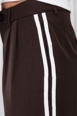 Close-up of dark brown trousers with two vertical white stripes down the side, worn with a white top.