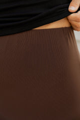 Close-up of a person lifting a black top to reveal a brown skirt or pants, with a hand pulling the fabric at the waistband.
