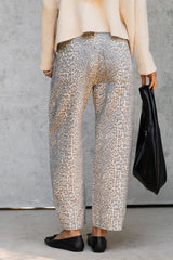 A person shown from the back wearing loose, wide-leg cropped trousers with an allover leopard-style print in beige and gray, paired with black flats and holding a black handbag against a textured gray wall.