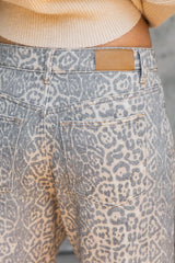 Close-up of the back waistband and pockets of high-waisted denim jeans featuring a gray and beige leopard print pattern, worn with a cream ribbed knit top.