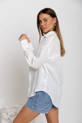 Woman wearing a white oversized shirt and denim shorts against a plain background