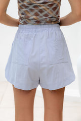 Back view of a person wearing light blue high-waisted shorts with an elastic waistband and two large patch pockets, paired with a brown patterned top.