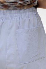 Close-up of a light blue-gray fabric garment with an elastic waistband and a large front patch pocket, shown on a person wearing a patterned top.