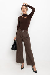 Woman wearing a brown long-sleeve top and wide-leg pants, holding a black handbag on a white background.
