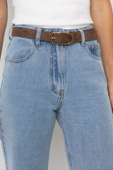 Person wearing blue jeans with a brown belt and white shirt on a plain background