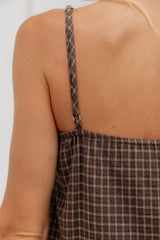 Close-up back view of a person wearing a brown plaid spaghetti-strap top or dress, showing the thin straps and fabric pattern against a light neutral background.