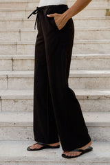 Black wide-leg drawstring pants worn by a model standing on light-colored stone steps, paired with black flip-flops.