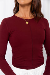 Woman wearing a burgundy long-sleeve top with white drawstring pants, carrying a burgundy bag, on a white background.