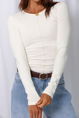 Woman wearing a white long-sleeve top with light-wash wide-leg jeans and a brown belt, carrying a brown handbag, on a white background.