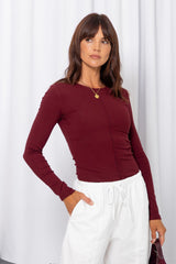 Woman wearing a burgundy long-sleeve top with white drawstring pants, carrying a burgundy bag, on a white background.