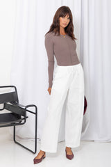 Woman wearing a taupe long-sleeve top with white drawstring pants, on a white background.