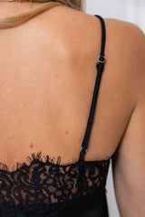 Close-up back view of a person wearing a black lace camisole or lingerie top with thin adjustable shoulder straps and a small silver metal adjuster.