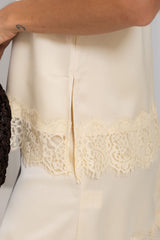 Close-up of a cream-colored satin or silk garment with a wide floral lace trim along the hem, shown on a model.