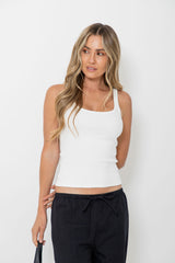 A woman modeling a white ribbed tank top with a square neckline and black drawstring pants, standing against a plain white studio background.