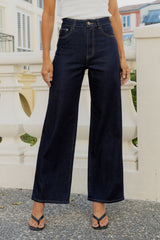A person wearing dark navy wide-leg cropped jeans with a white top and black thong sandals, standing outdoors in front of a white balustrade railing.