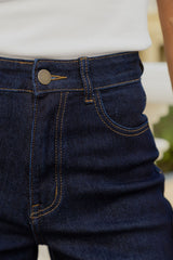 Close-up of a person wearing dark indigo blue denim jeans with gold contrast stitching and a white ribbed top.