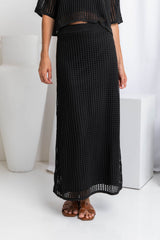A model wearing a midi length black crochet knit skirt with a ribbed elastic waistband and fitted silhouette.