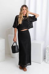 A model wearing a crochet knit black top with a midi length black crochet knit skirt with a ribbed elastic waistband and fitted silhouette.