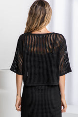 A woman wearing a black crochet knit crop top with a scoop neckline and 1/4 sleeve, paired with a black skirt.