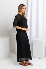 A woman wearing a black crochet knit crop top with a scoop neckline and 1/4 sleeve, paired with a black skirt.