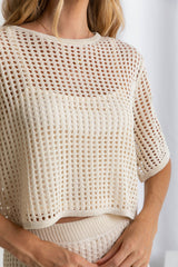 A female model wearing a beige crochet crop top with a scoop neckline and 1/4 sleeves.
